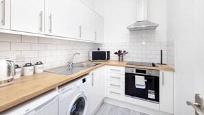 A compact kitchen with white cabinets, a microwave, a sink, a stove, and a washing machine. - Argyl | Charming 2-Bedroom Apt. on Thistle Street (Edinburgh)