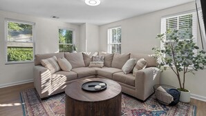 A modern living room with a beige sectional sofa, a round coffee table, and a large window with blinds.