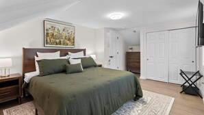 A bedroom with a large bed, a nightstand, a dresser, and a TV.