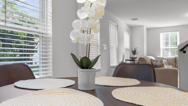 A dining area with a wooden table, white placemats, and a potted orchid.