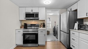 A modern kitchen with white cabinets, stainless steel appliances, and a wooden floor.