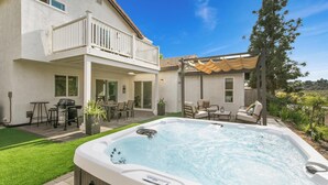 Una casa de dos plantas con un patio, un jacuzzi y mobiliario exterior.