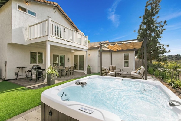 A two-story house with a patio area, a hot tub, and outdoor furniture.