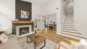 A spacious living room with a fireplace, a dining area, and a staircase leading to an upper level.