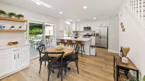 A modern kitchen with white cabinets, a central island, and a dining area with wooden chairs.