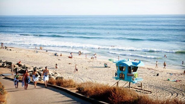 A beach with a lifeguard station, people walking, and the ocean.