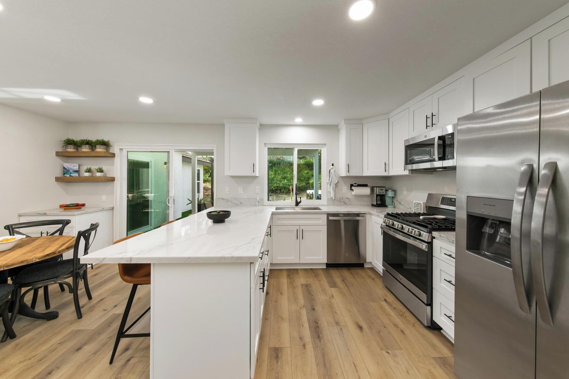 A modern kitchen with white cabinets, stainless steel appliances, and a wooden dining table.