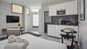 Una habitación de hotel moderna con cama, televisión, escritorio, kitchenette y zona de comedor.