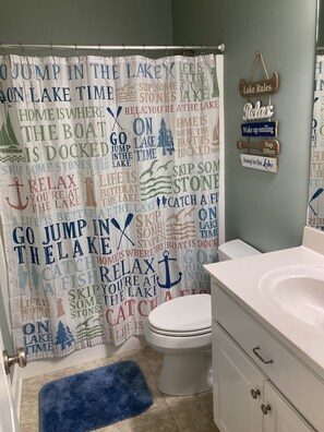 Un baño con cortina de ducha con motivos náuticos y una alfombra pequeña.