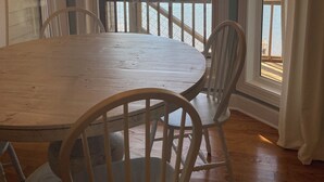 Een eetgedeelte met een grote houten tafel en witte stoelen, grote ramen met uitzicht op een meer, en een kroonluchter aan het plafond.