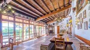 A spacious dining area with wooden furniture, large windows, and a high ceiling with exposed beams.