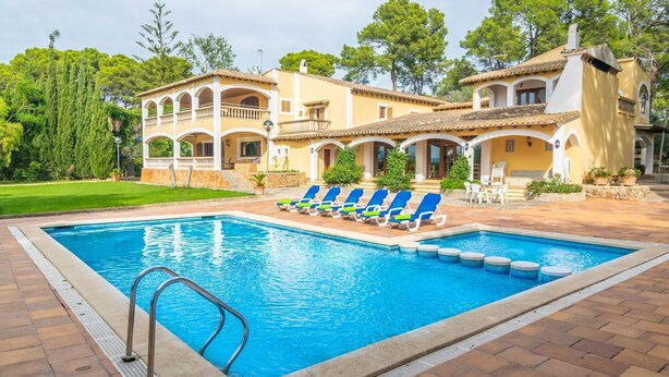 A swimming pool with lounge chairs, a covered patio, and a building with arches and balconies.