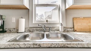 Una cocina con un lavamanos doble de acero inoxidable, una ventana sobre el lavamanos y una tabla de cortar de madera en la encimera.