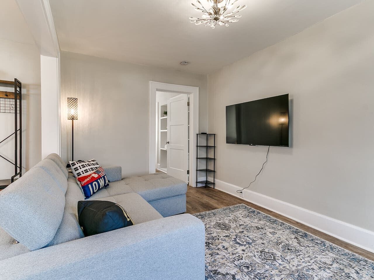 Un salon moderne avec un canapé d’angle, un téléviseur à écran plat fixé au mur, un tapis à motifs et une lampe sur pied.