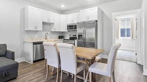 Una cocina moderna con armarios blancos, electrodomésticos de acero inoxidable y una mesa de comedor de madera con cuatro sillas.