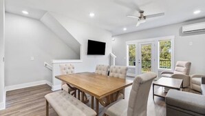 Amplia habitación con una mesa de comedor de madera, sillas acolchadas, un ventilador de techo y un ventanal con vistas a zonas verdes.