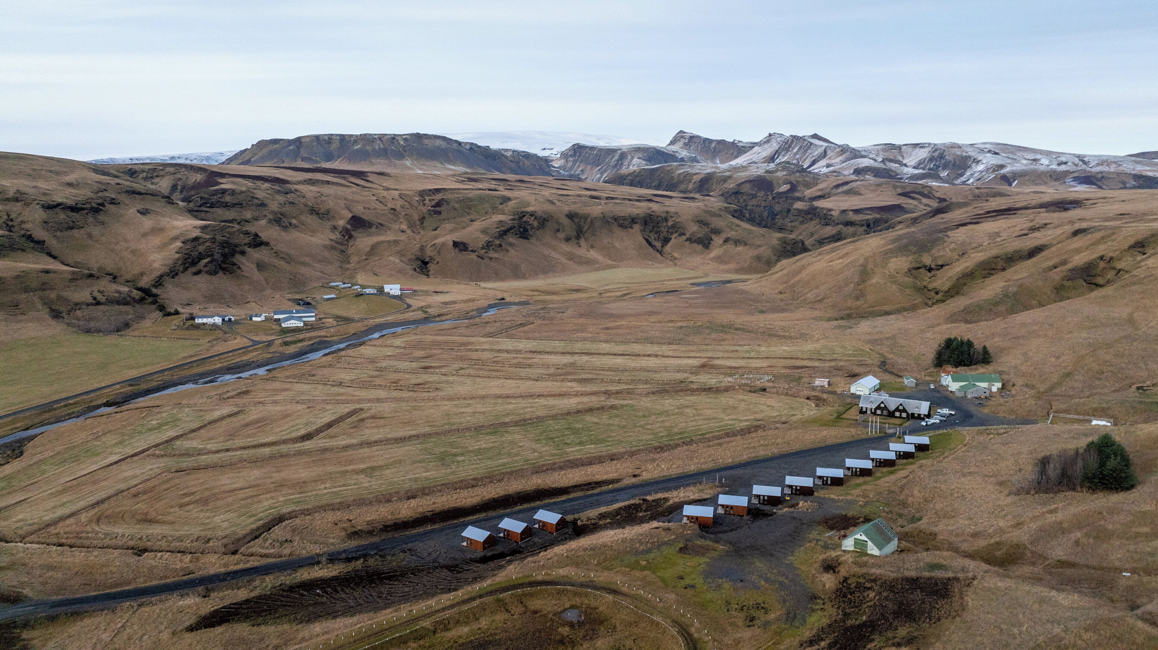 An aerial view of a rural area with a series of small buildings, a road, and a river.