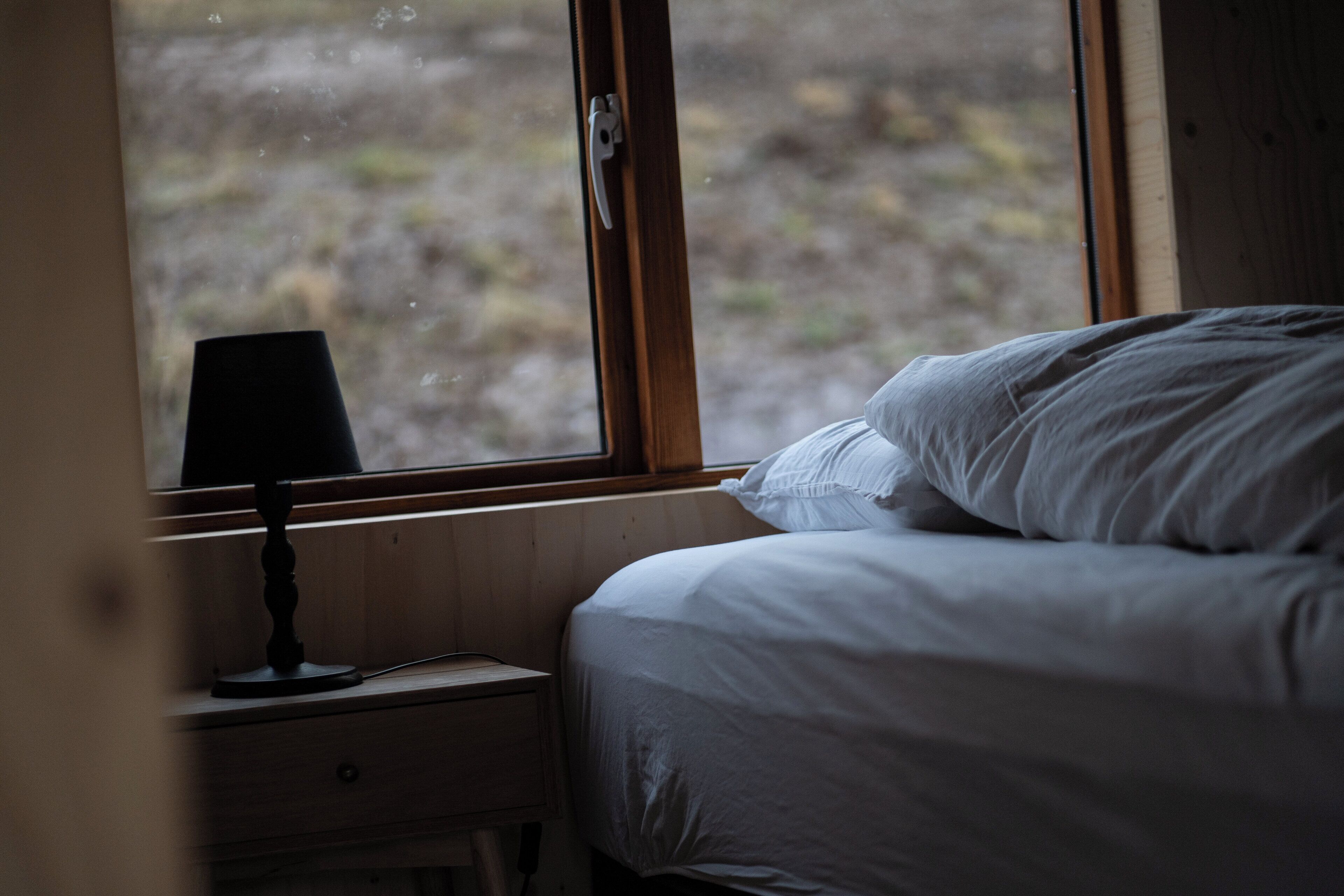 Un dormitorio con cama, mesita de noche, lámpara y ventana con vistas al exterior.