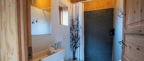 Un baño pequeño con techo de madera, un lavamanos blanco, un inodoro y una cortina de ducha con diseño de árbol.