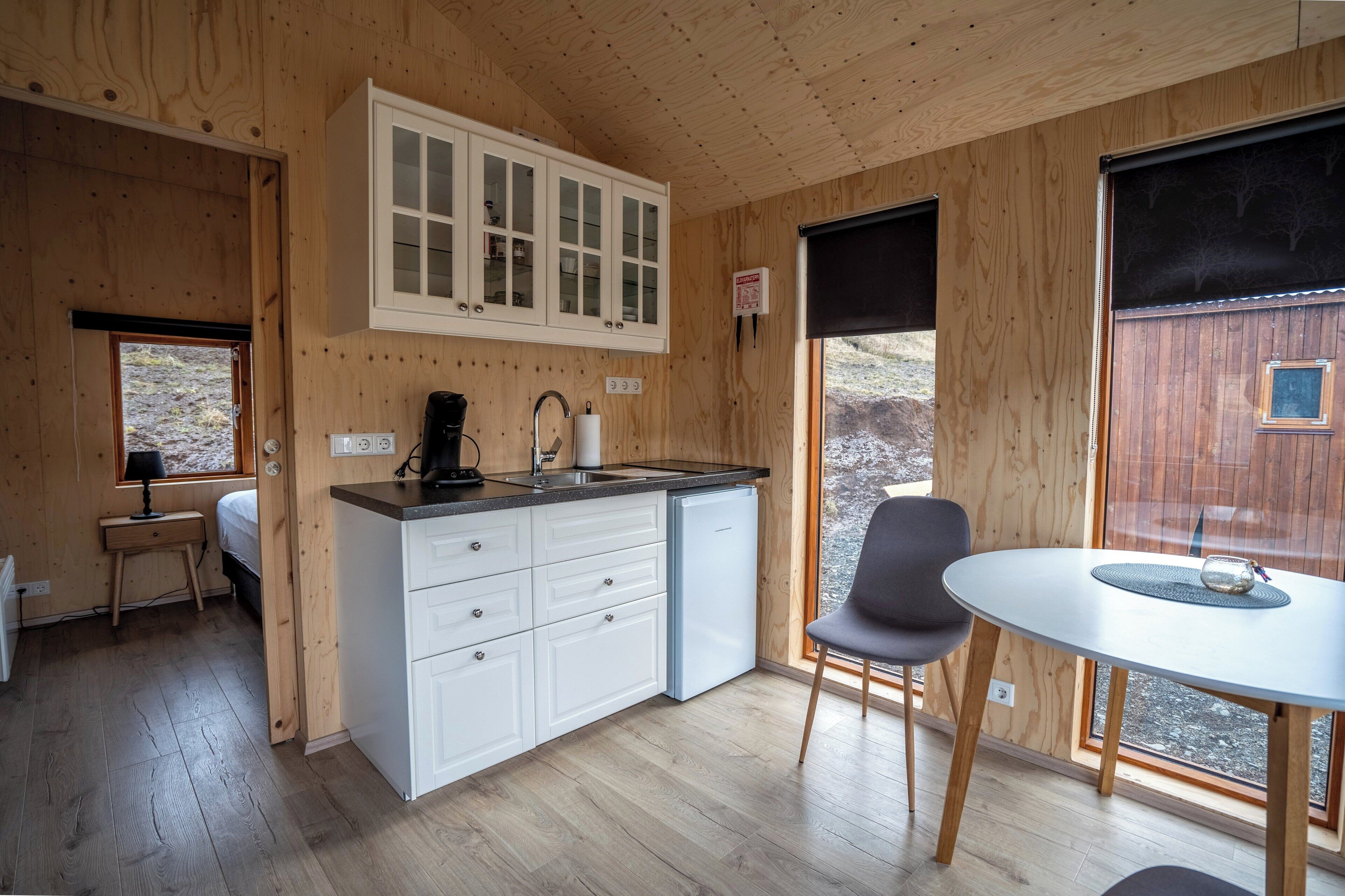 Una cabaña de madera compacta con kitchenette, comedor y ventana con vistas al exterior.