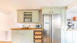 A kitchen with a double-door refrigerator, a microwave, and a bread box on the counter. There are wicker baskets under the counter and a window above the cabinets. - Stanley Road - Gorgeous Modern Flat in Oxford (Oxford)