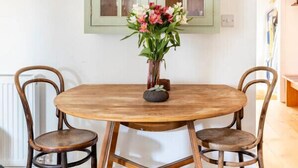 A dining area with a round wooden table, two chairs, and a green cabinet with glass doors. - Stanley Road - Gorgeous Modern Flat in Oxford (Oxford)