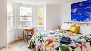 A bedroom with a large bed, a window seat, and a painting of birds. - Stanley Road - Gorgeous Modern Flat in Oxford (Oxford)