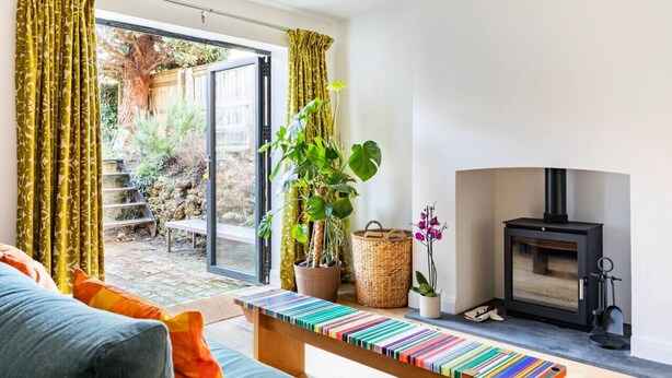 A living room with a sofa, a colorful striped bench, a fireplace, and a large window with curtains. - Stanley Road - Gorgeous Modern Flat in Oxford (Oxford)