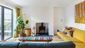 A modern living room with a sofa, a bench, a fireplace, and a large window. - Stanley Road - Gorgeous Modern Flat in Oxford (Oxford)