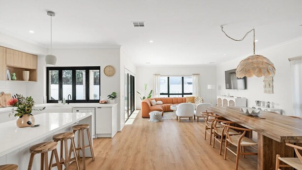 Una cocina moderna con una isla central, suelo de madera y un comedor con una mesa larga y sillas.
