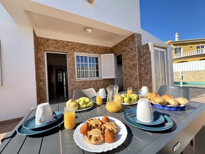 Een terras met een ontbijttafel, compleet met fruit, gebak en sap.