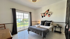 Een hotelkamer met een bed, een bureau, een stoel, een nachtkastje, een potplant en uitzicht op de omgeving.