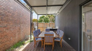 A covered patio with a table and chairs, a brick wall, and a wooden fence. - Inlet Paradise in Rhyll (Rhyll)