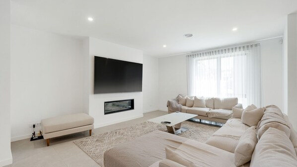 A modern living room with a flat-screen TV mounted on the wall, a beige sofa set, a coffee table, and a patterned rug. - Inlet Paradise in Rhyll (Rhyll)