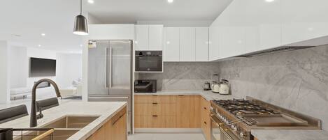 A modern kitchen with a central island, stainless steel appliances, and a marble backsplash.