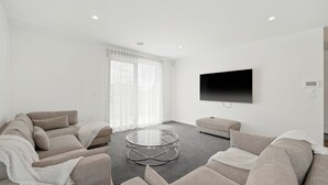 A modern living room with a sofa set, a glass coffee table, and a flat-screen TV mounted on the wall. - Inlet Paradise in Rhyll (Rhyll)