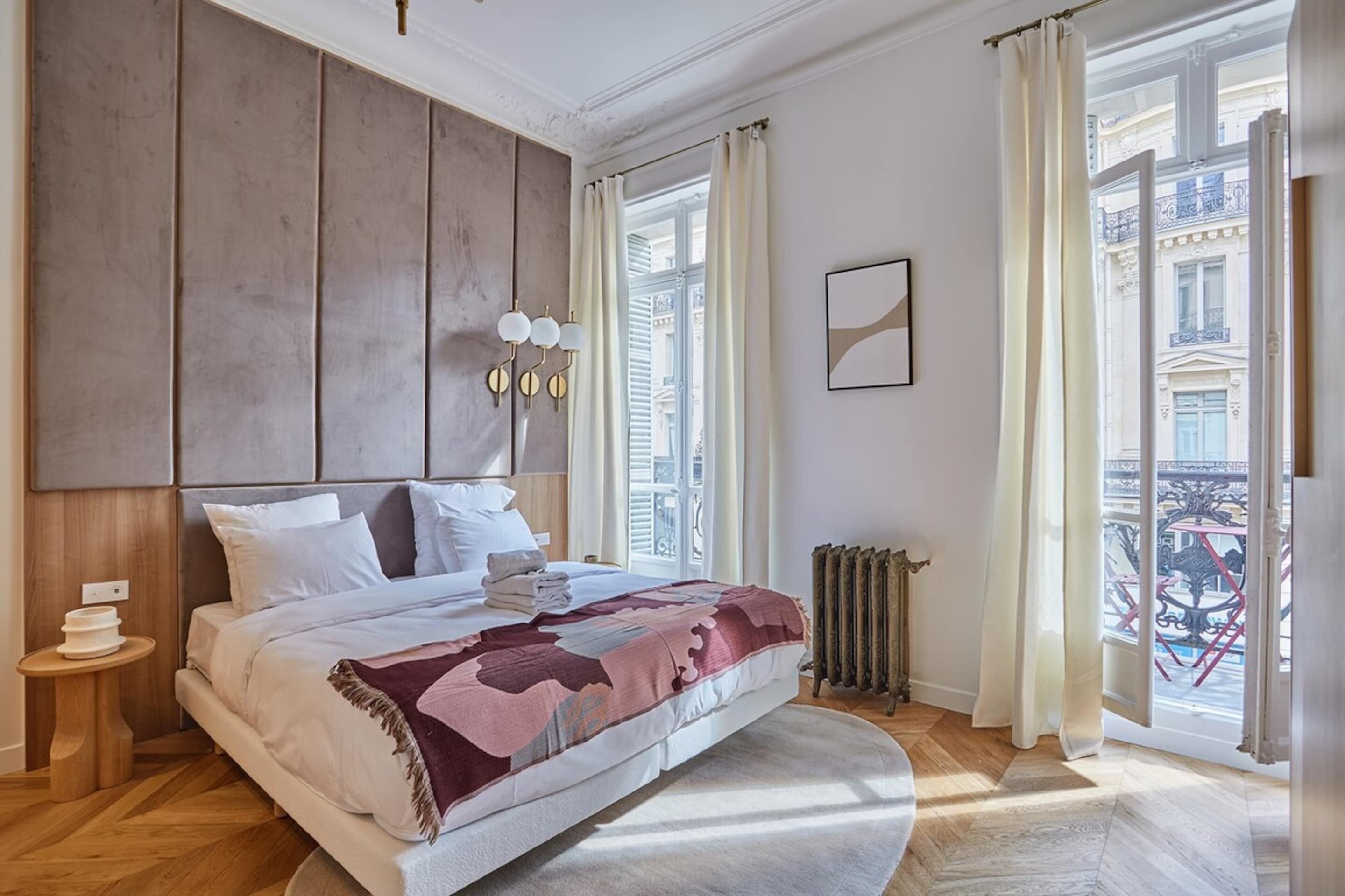 A bedroom with a large bed, a radiator, a window with curtains, and a view of the outside.