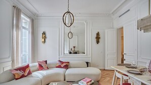 A living room with a beige sectional sofa, a coffee table, a dining table with chairs, and a chandelier. - 4 Rooms Apartment Opera Vendome (Paris)