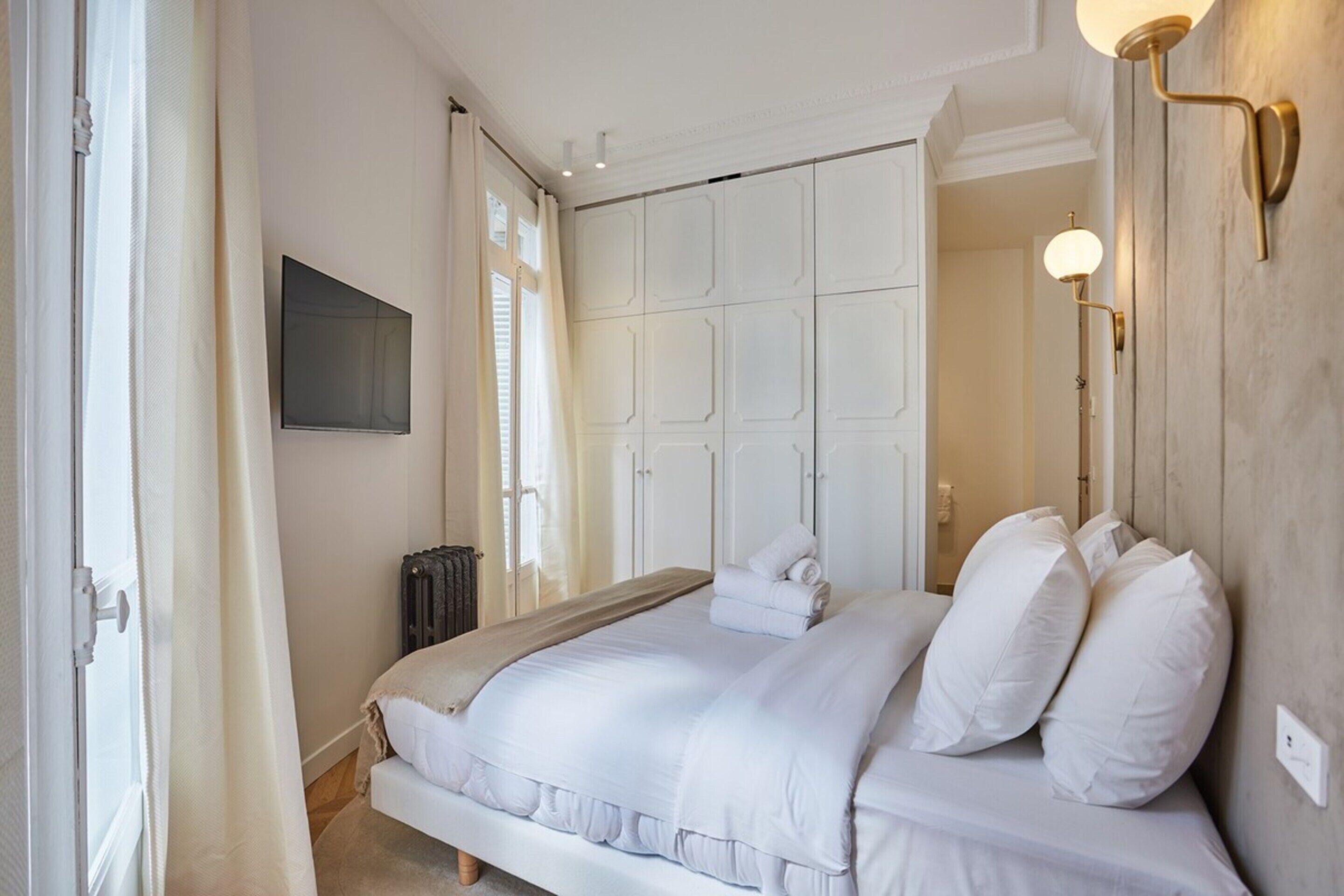 A bedroom with a large bed, a wardrobe, a radiator, and a wall-mounted light fixture.