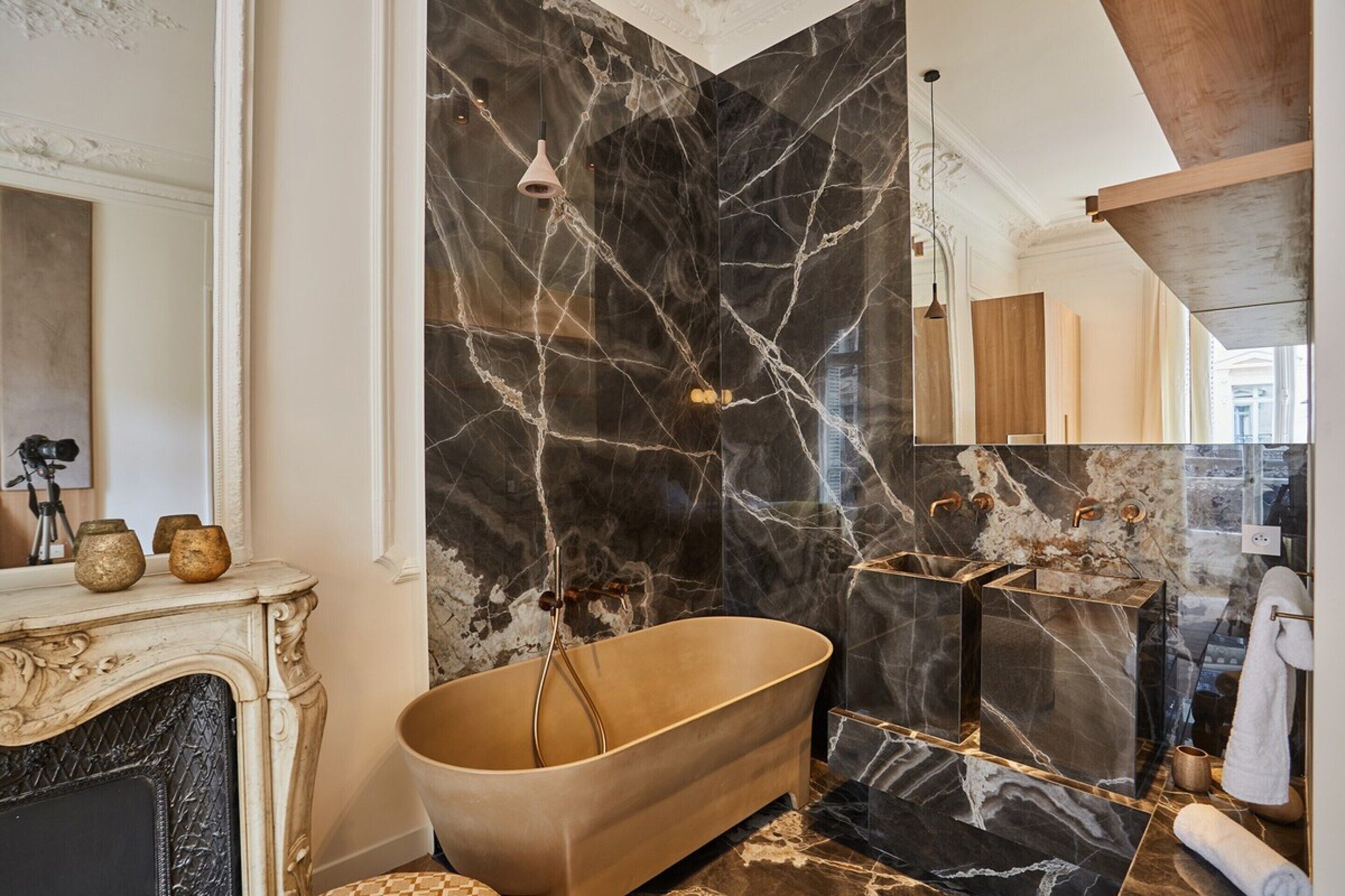 A luxurious bathroom with a freestanding bathtub, marble walls, and a classic fireplace.