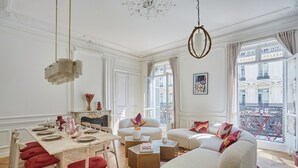 A spacious living room with a dining area, large windows, and a view of the city. - 4 Rooms Apartment Opera Vendome (Paris)