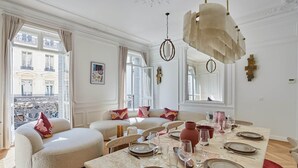 A dining room with a marble table set for six, a sofa with cushions, and a view of the city. - 4 Rooms Apartment Opera Vendome (Paris)