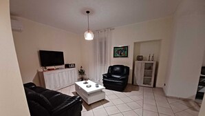 Un salon comprenant un canapé en cuir noir, une table basse blanche, un fauteuil en cuir noir, un téléviseur à écran plat fixé au mur et un meuble avec des portes en verre.