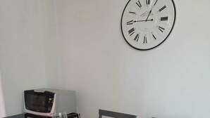 Une table à manger dressée avec des assiettes, des couverts et des verres à vin, et une horloge murale au-dessus.