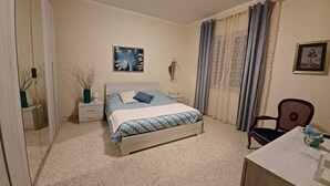 Une chambre à coucher comprenant un lit, une table de chevet, une chaise, un bureau et un miroir.