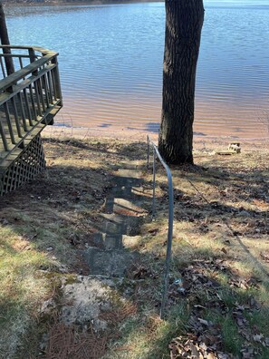 Une terrasse en bois qui mène à une plage rocheuse, au bord d’un lac paisible.