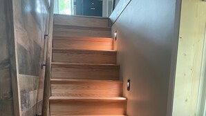 Een houten trap met een leuning, een lichtschakelaar en een raam aan de rechterkant.