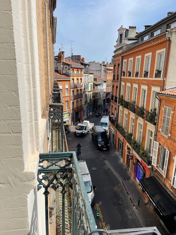 A narrow street with buildings on either side, featuring balconies and a variety of architectural styles.
