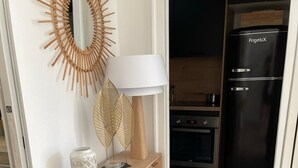 Et træbord med en hvid lampe, dekorative blade og en mønstret vase. En sort køleskab og et træskab ses i baggrunden.