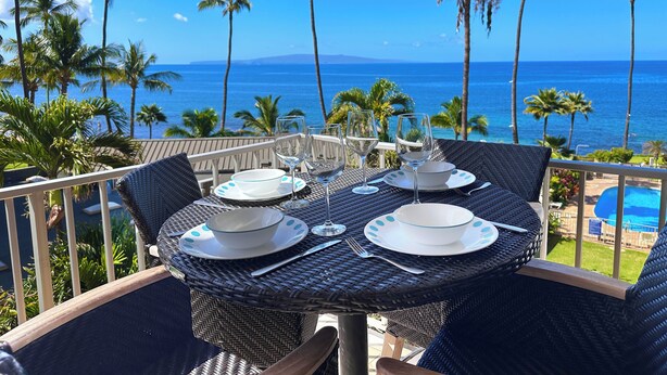 A dining table with plates, glasses, and cutlery set on a balcony overlooking a pool and the ocean. - Nestled Between Two Beaches Kihei Oceanview 2BR Condo Panoramic Views Pool (Kihei)